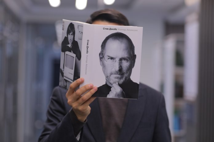 a man holding up a book with a picture of steve jobs on it