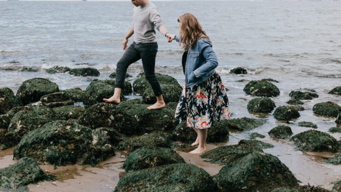 man and woman holding hand together while stepping on rocks near sea