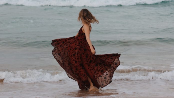 woman in black and red floral dress standing on seashore during daytime