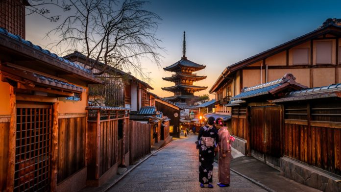 two women in purple and pink kimono standing on street