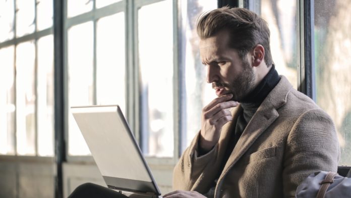 man holding his chin facing laptop computer