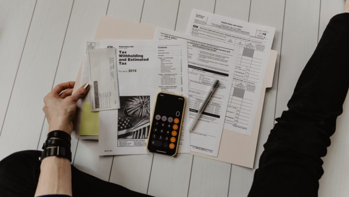 person holding paper near pen and calculator