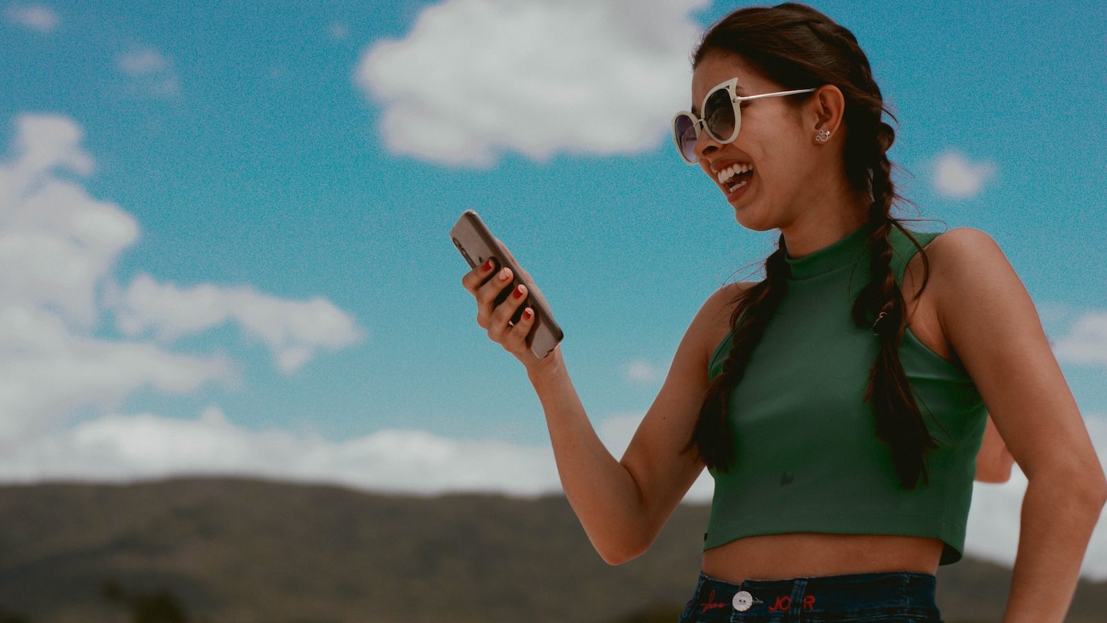 woman in green tank top holding smartphone during daytime
