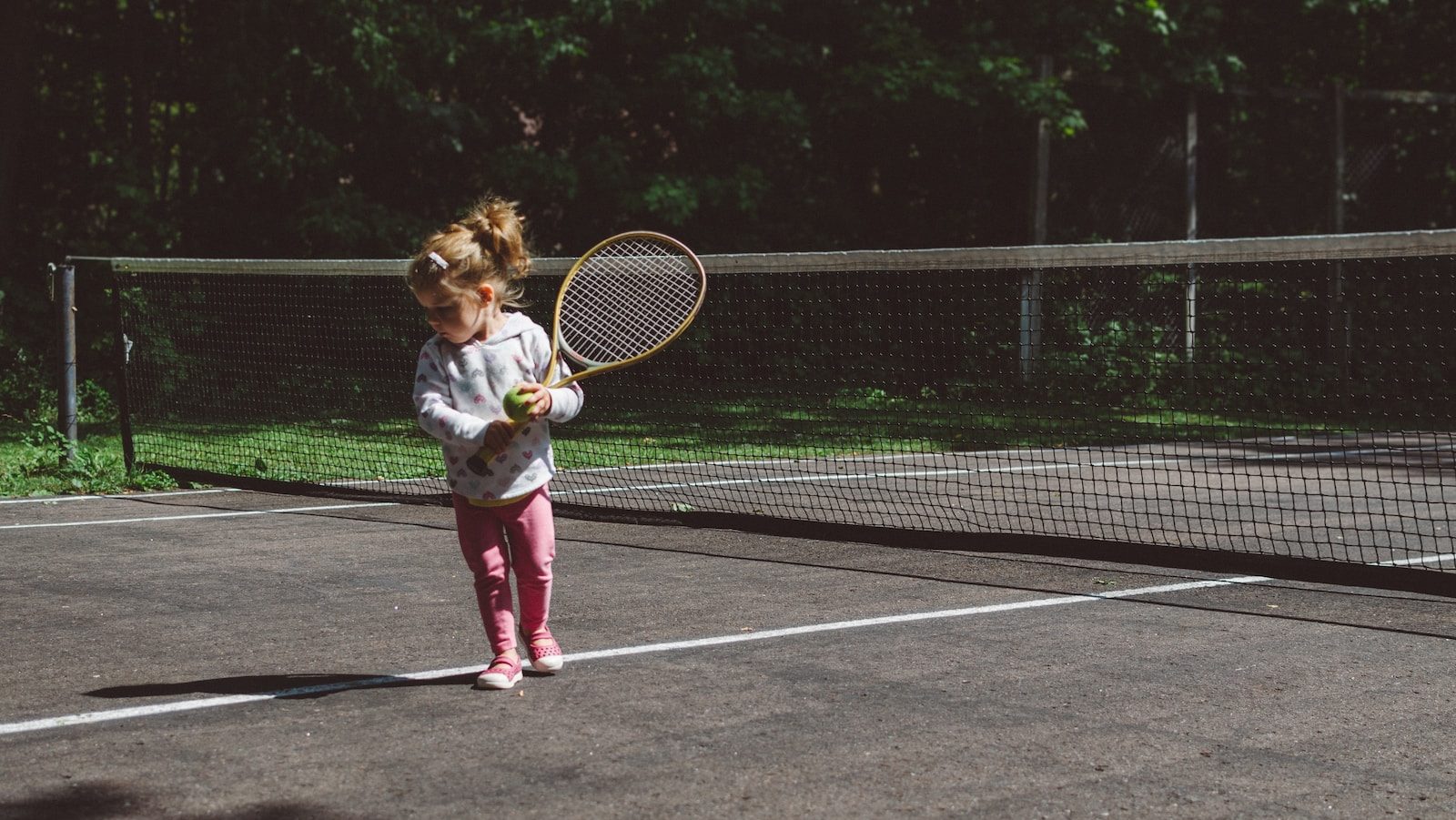 girl holding lawn tennis racket while standing beside white and black net